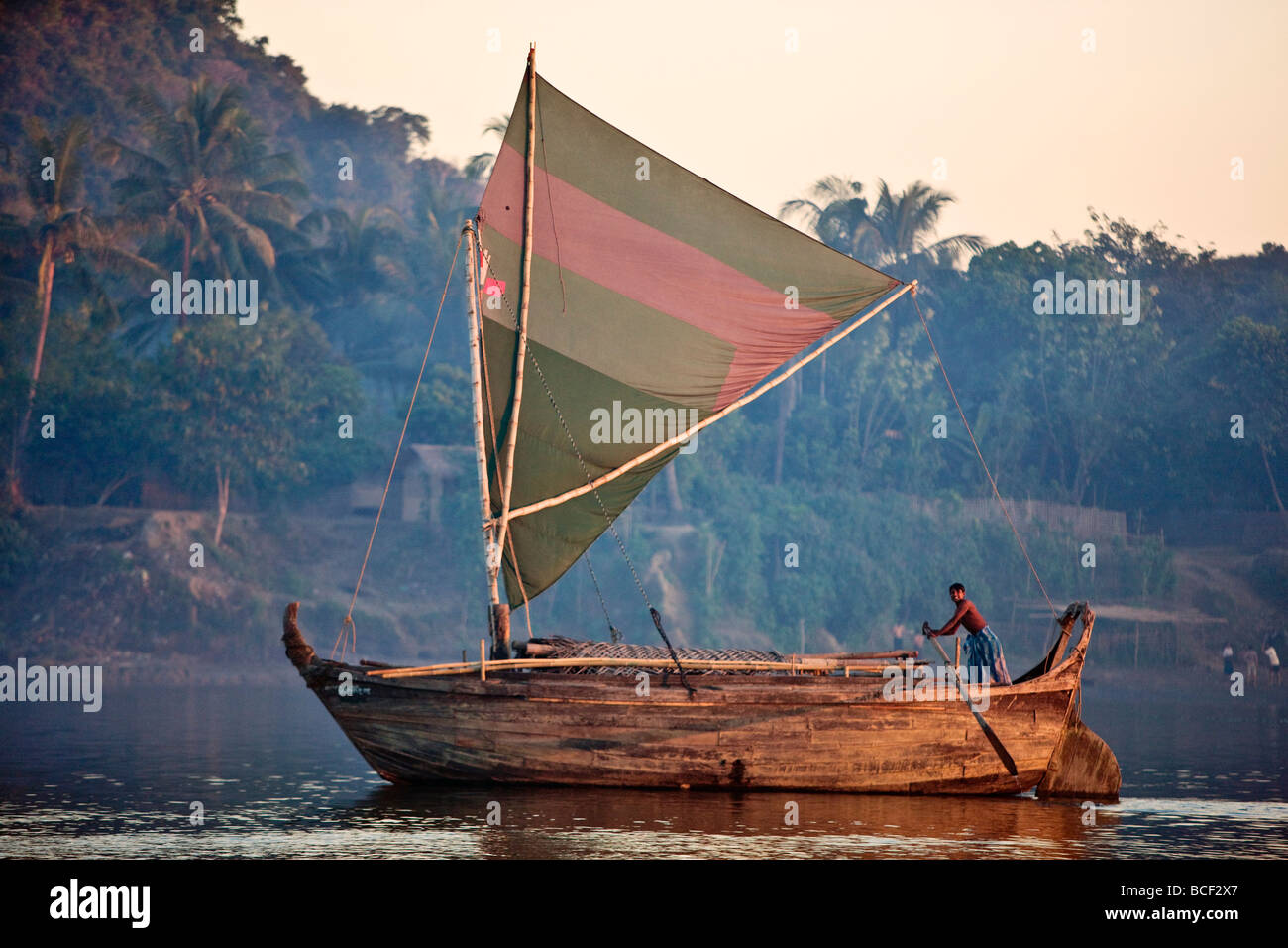 Una grande barca in legno di design Rakhine vele fino il lay Myo nel fiume allo sbiadimento della luce della sera. Foto Stock