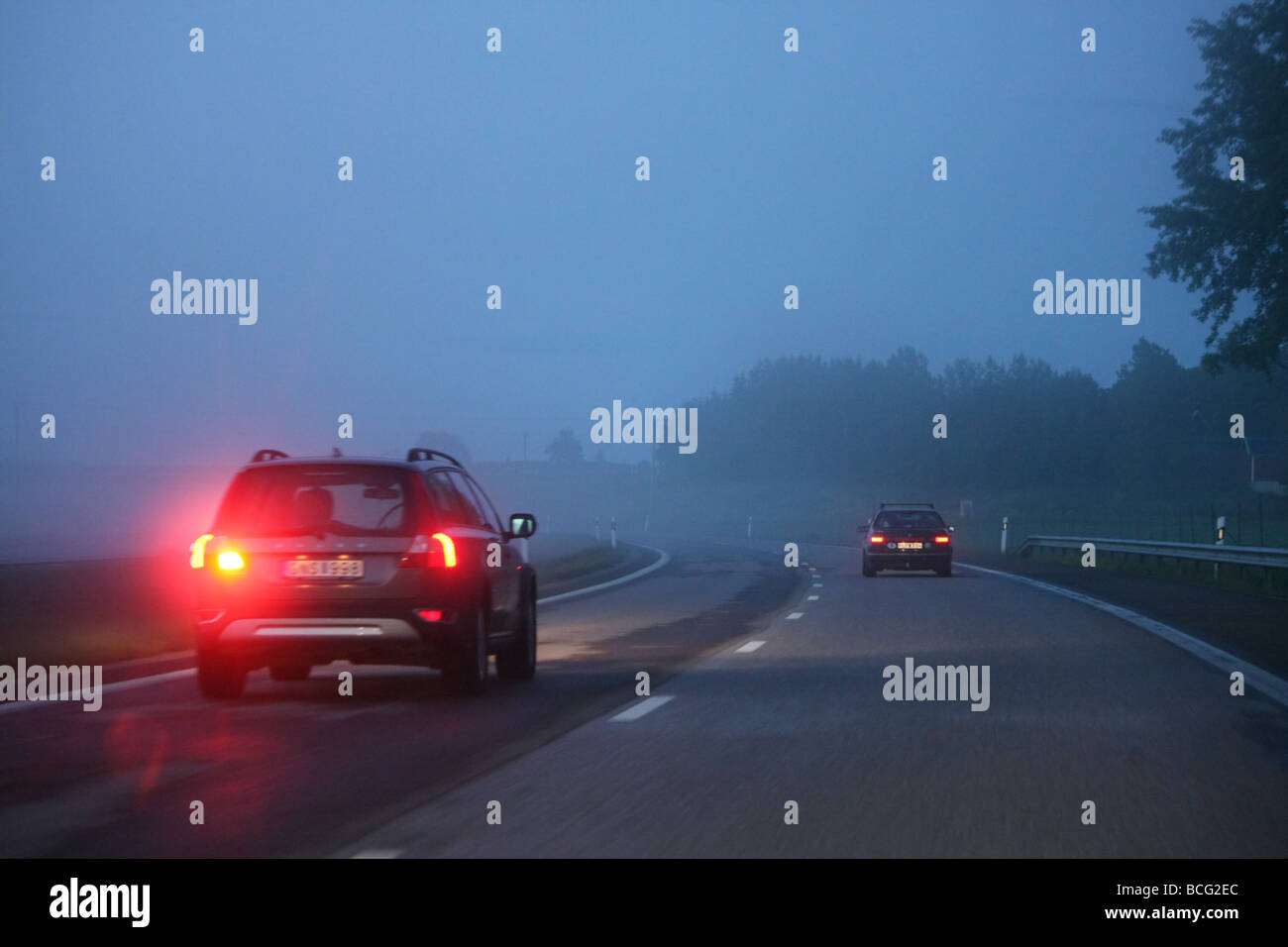 Auto su un buio, foggy autostrada con la nebbia spia accesa. Foto Stock