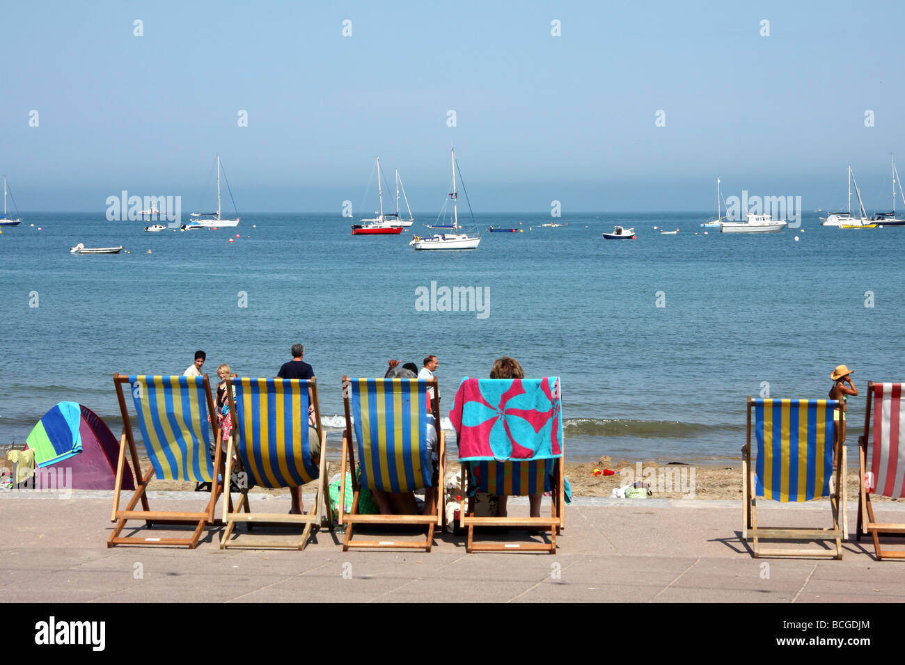 La gente seduta in sedie a sdraio che guarda al mare a Swanage, Dorset, Regno Unito Foto Stock