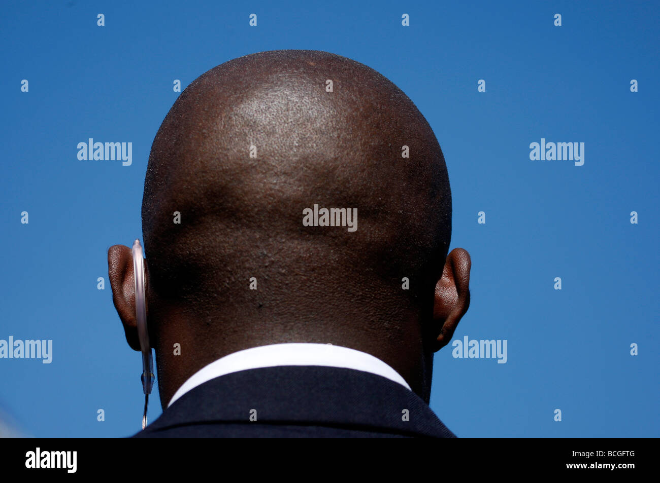 Retro della testa pelata di un nero guardia di sicurezza contro un cielo blu chiaro Foto Stock
