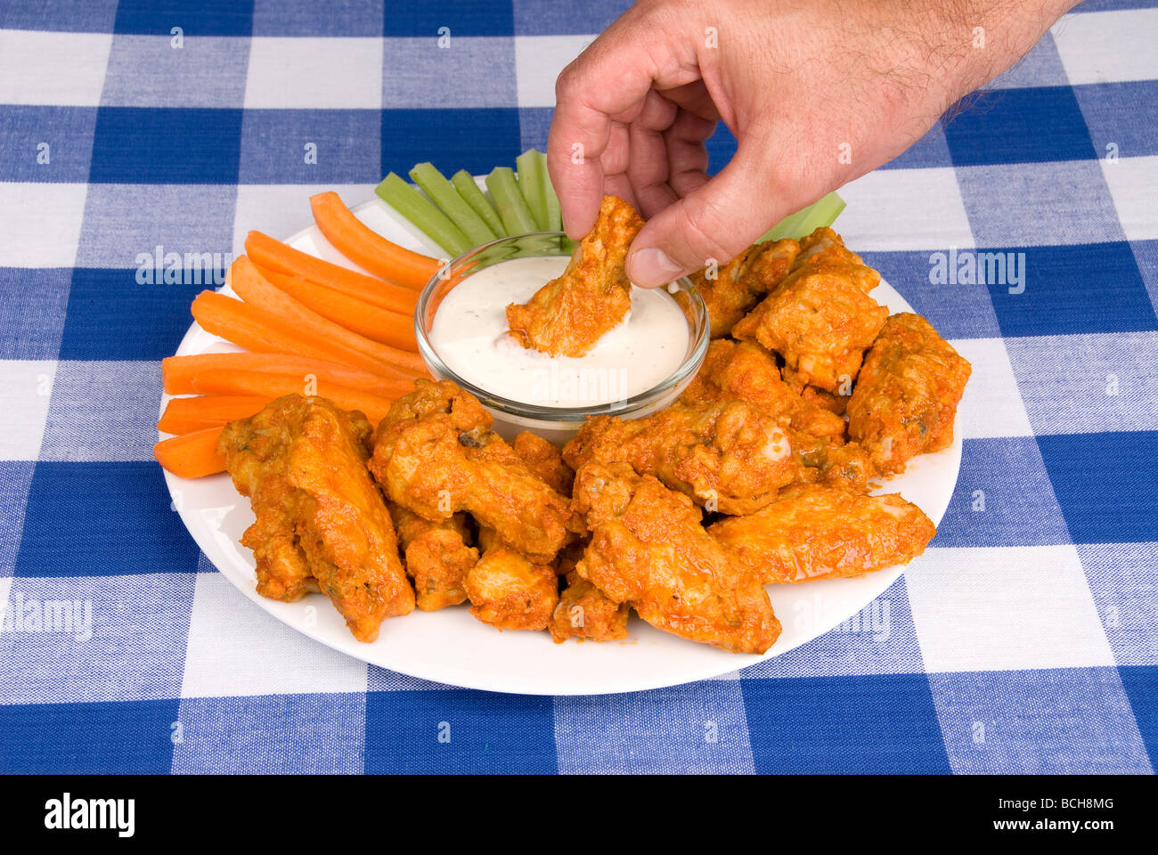 Un piatto di pollo ali a caldo il sedano e le carote con salsa di immersione attira un uomo che bagna un ala in alcuni gustosa salsa ranch Foto Stock