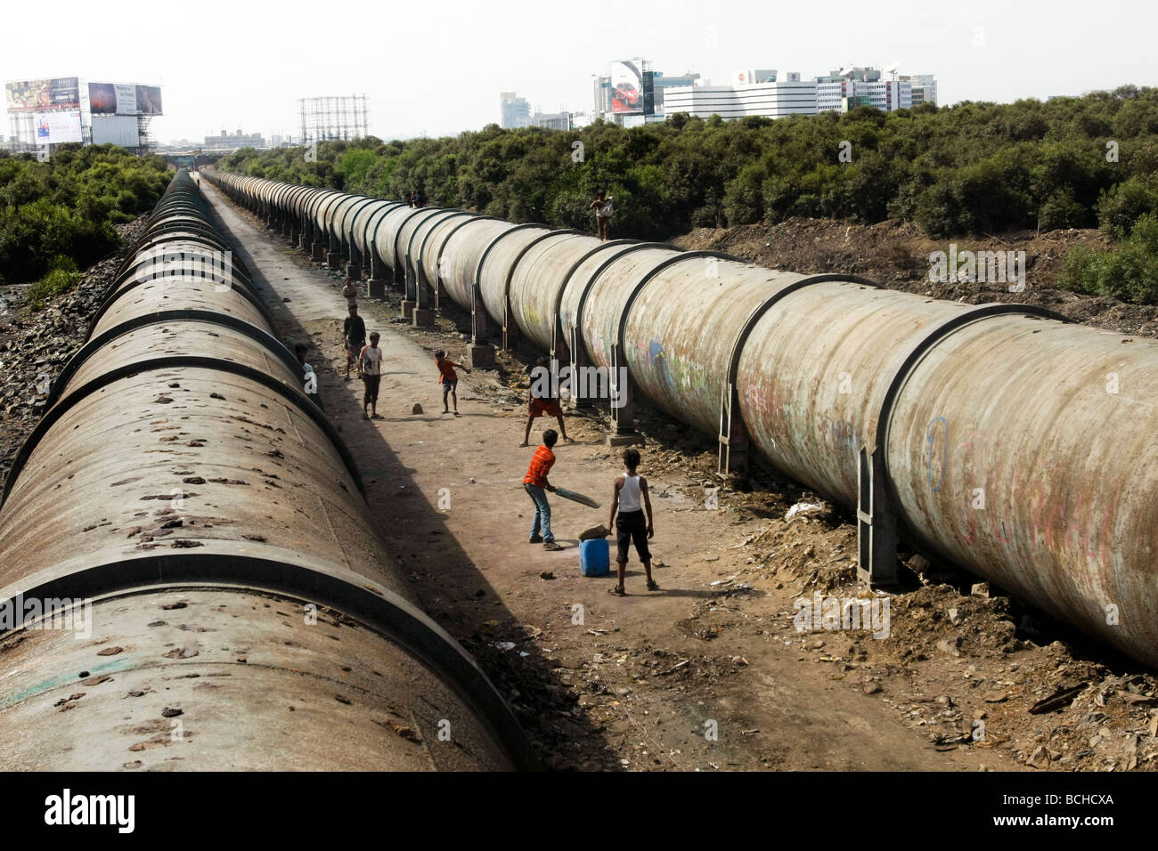 I bambini giocare a cricket tra due grandi waterpipes che corre attraverso Dharavi, la più grande delle baraccopoli di Mumbai (Bombay). Foto Stock