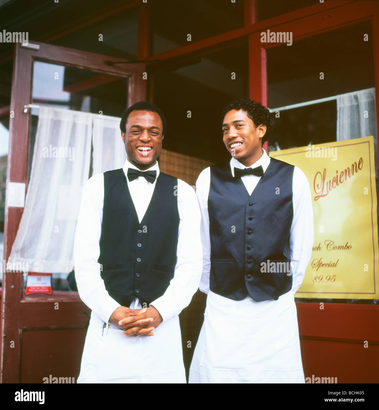 Due camerieri uomini neri in grembiuli e cravatte sorridenti salutano i clienti all'esterno del ristorante Chez Lucienne Harlem New York City, NY KATHY DEWITT Foto Stock