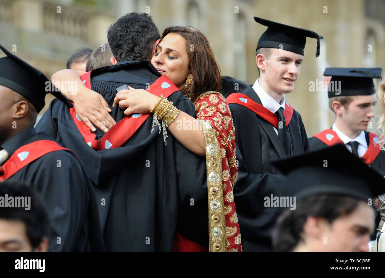 I diplomati sono abbracciati da membri della famiglia come laureati celebrano il loro giorno di graduazione presso una università britannica UK Foto Stock