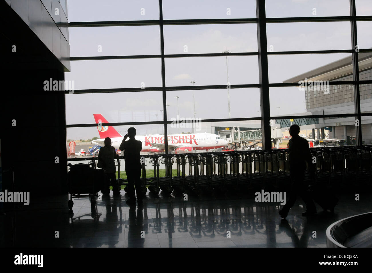 Passeggeri nella sala arrivi dell'aeroporto internazionale di Hyderabad orologi un piano Kingfisher parcheggiata fuori il terminale. Foto Stock