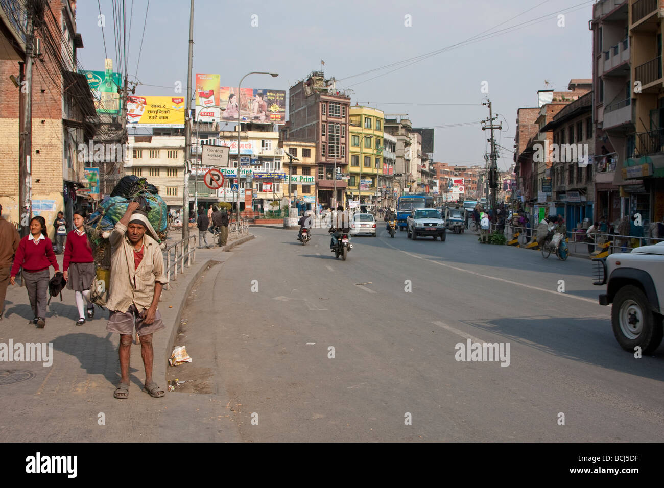 Kathmandu, Nepal. Scena di strada. Scuola ragazze in uniforme, operaio portano carichi pesanti, il traffico. Foto Stock