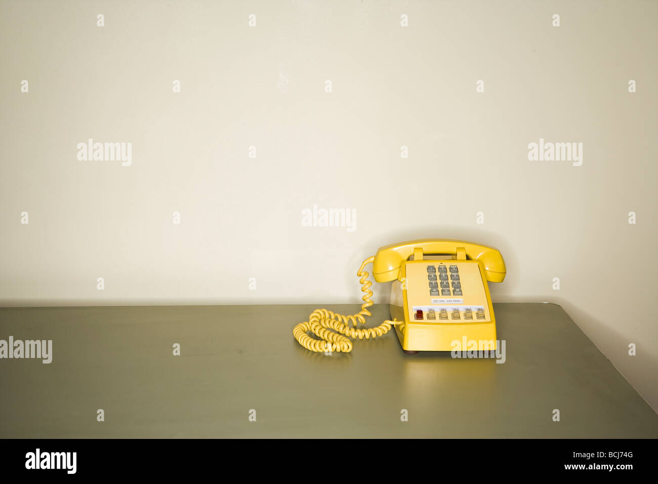 Giallo telefono a toni seduto sulla scrivania in metallo nella parte anteriore della parete bianca. Foto Stock
