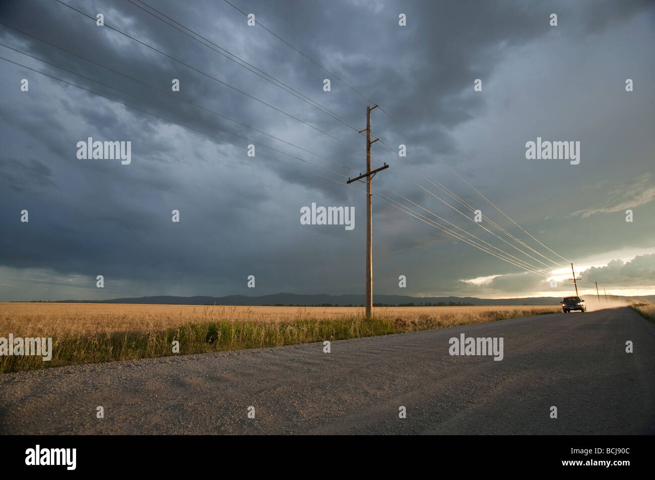 Carrello VEICOLO SUV automobile sulla sterrata strada di ghiaia rivestiti con poli di utilità al tramonto con drammatica sky Montana USA Foto Stock