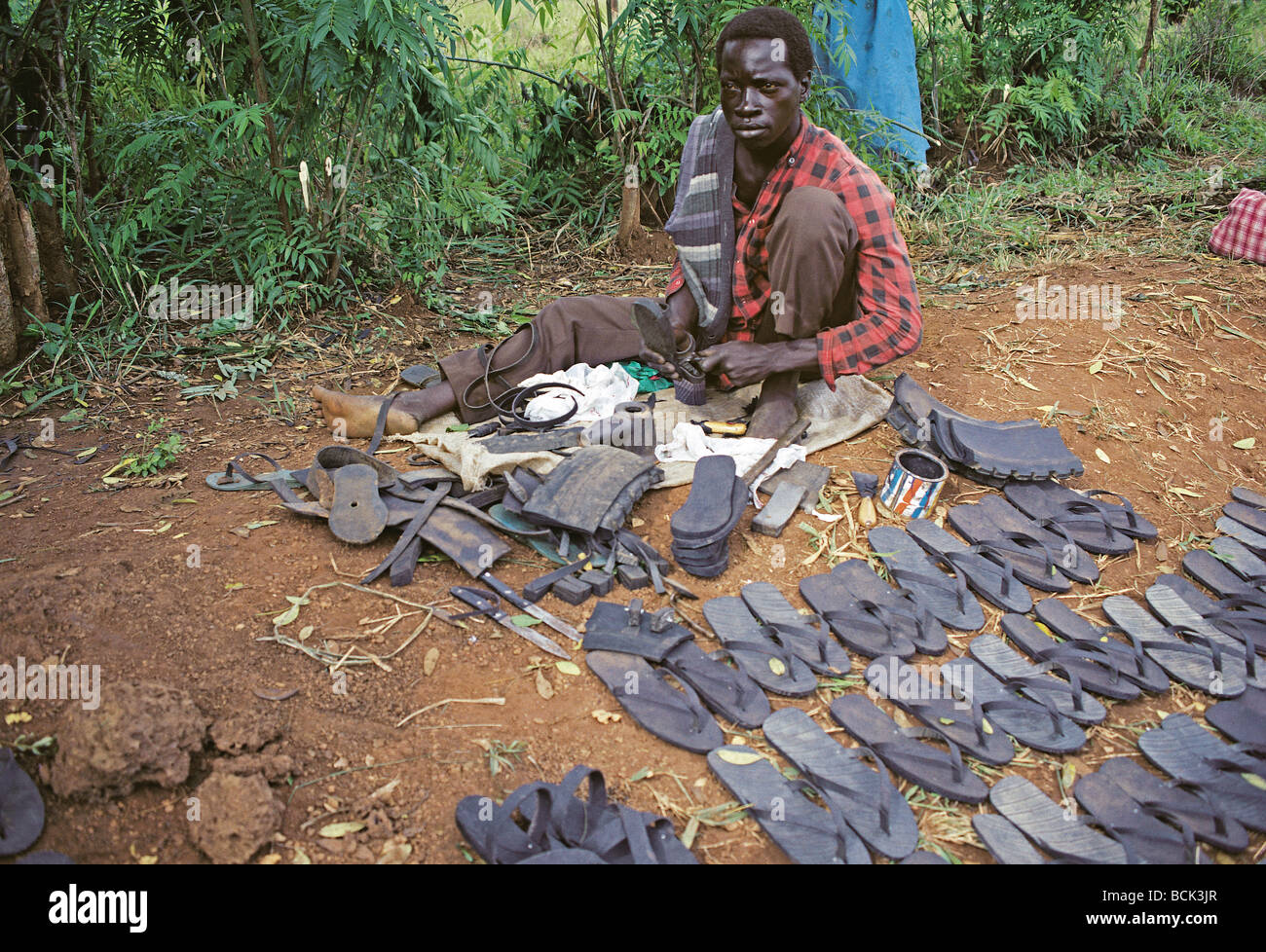 Uomo che fa il flip flop sandali da pneumatici in gomma in vendita presso Porta mercato Masindi Uganda Africa orientale Foto Stock