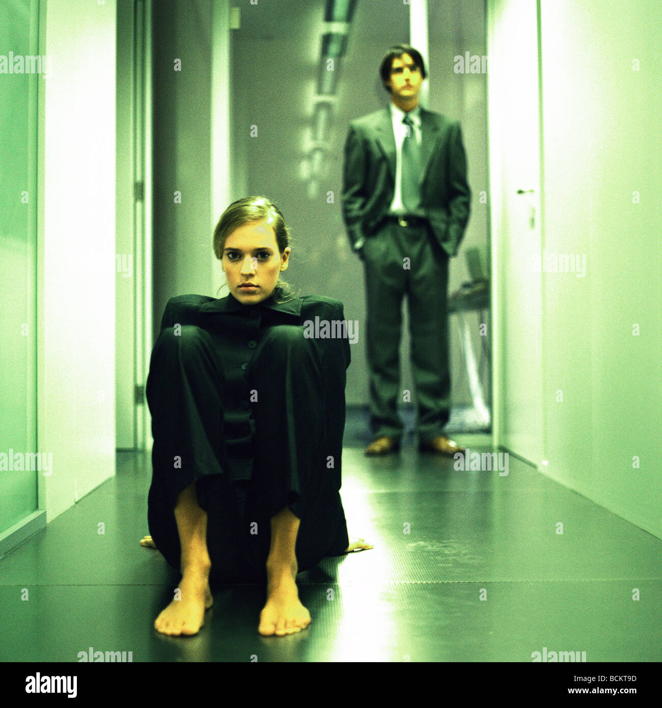 Donna seduta sul pavimento nel corridoio, uomo in piedi dietro Foto Stock