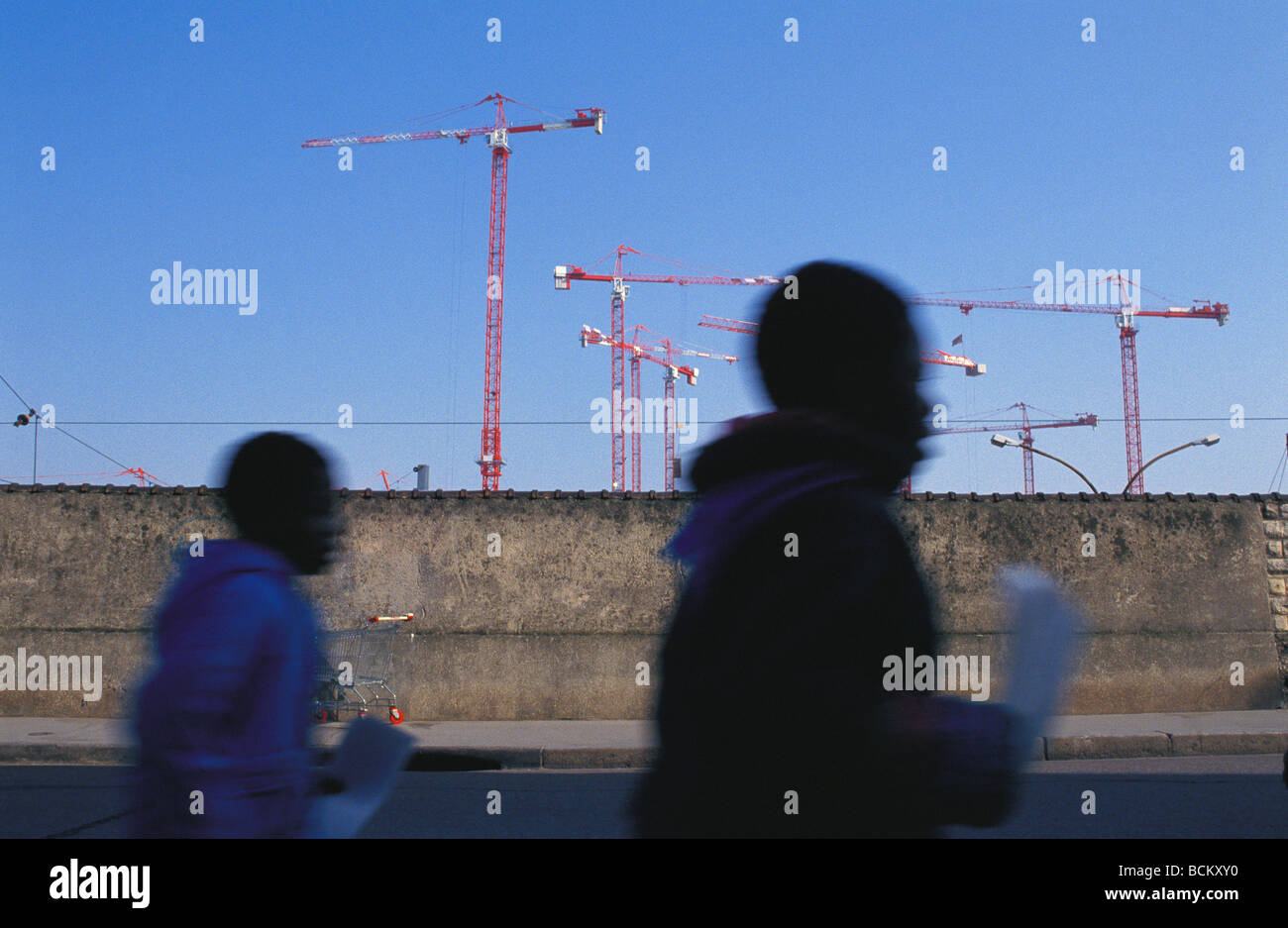 Sagome di persone a piedi nella parte anteriore della parete di cemento e gru Foto Stock