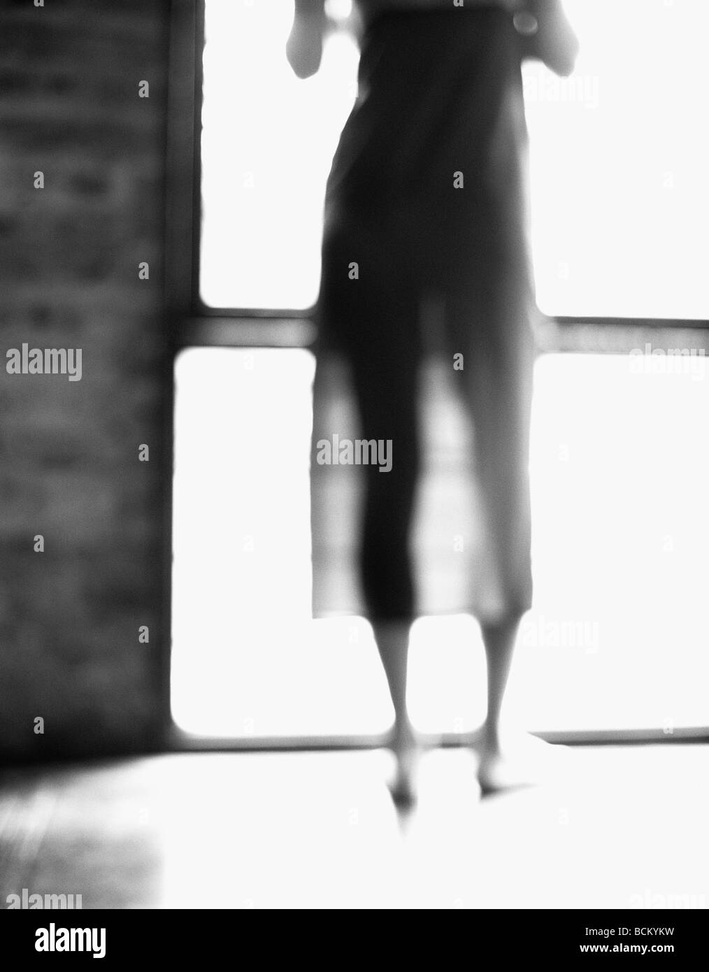 Giovane donna in piedi di fronte alla finestra, il torace verso il basso, vista posteriore, b&W, sfocato Foto Stock