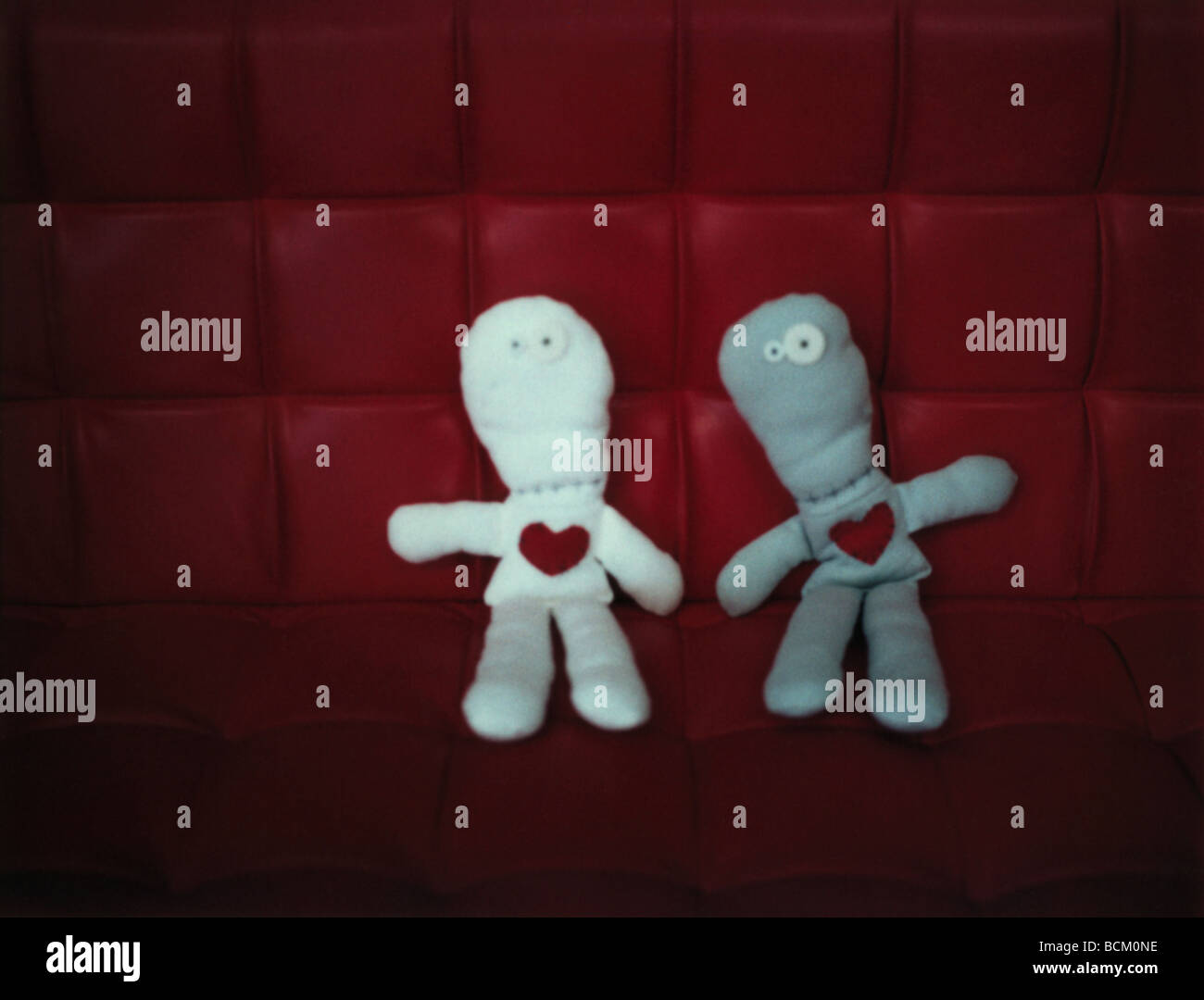 Due bambole di fianco a fianco sul divano rosso, vista frontale Foto Stock