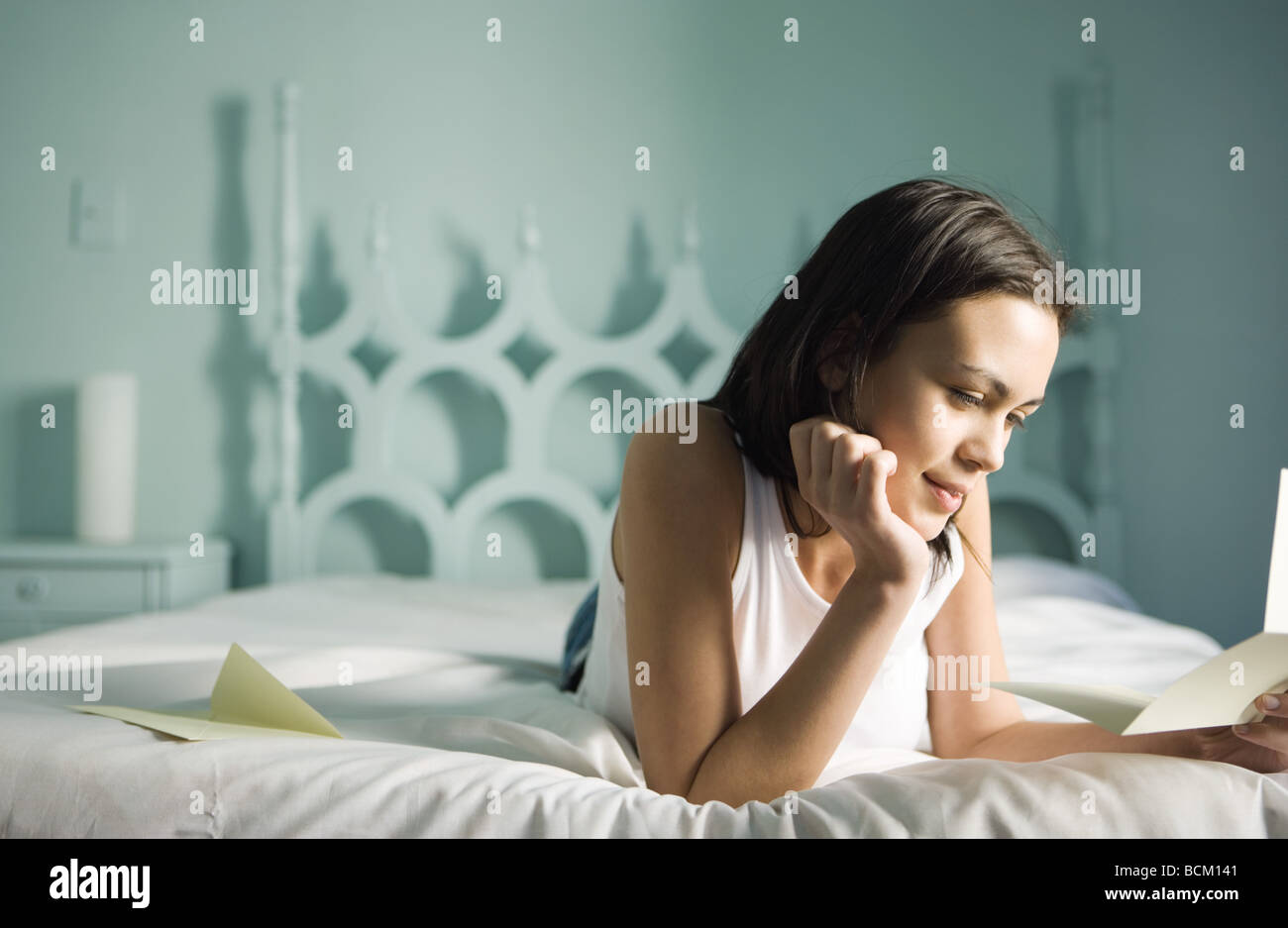 Donna sdraiata sul letto con la mano sotto il mento, lettura la lettera Foto Stock