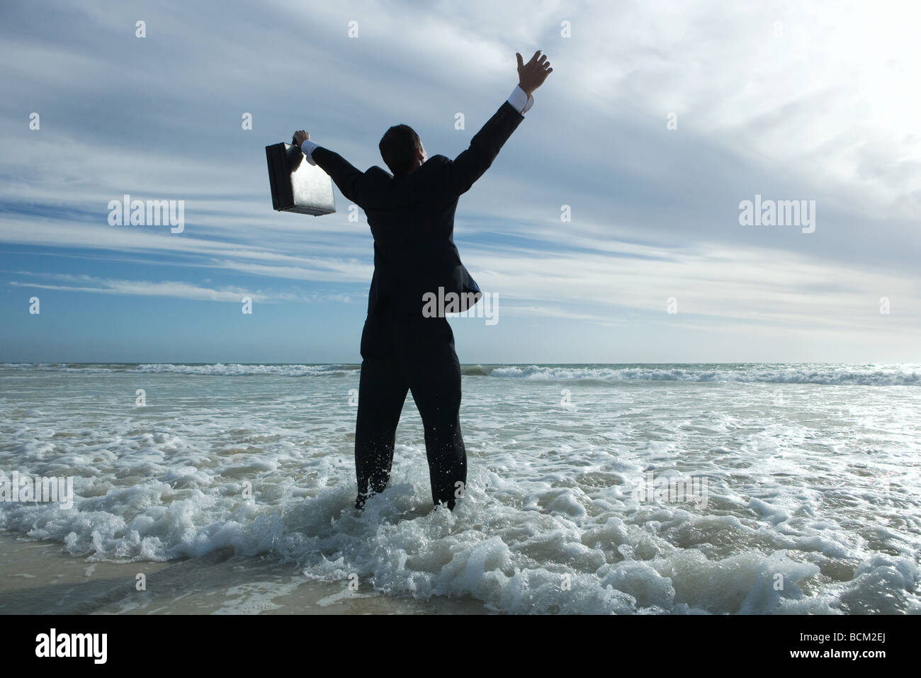 Imprenditore in piedi di surf in spiaggia, bracci sollevati, vista posteriore Foto Stock