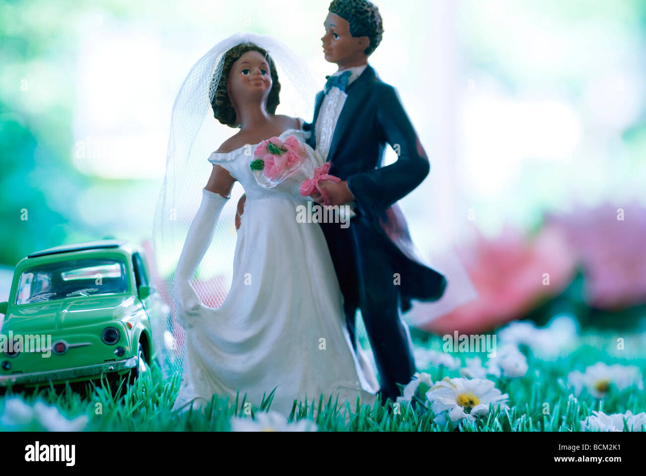 Plastica sposa e lo sposo in piedi nel campo dei fiori finti, giocattolo auto in background Foto Stock