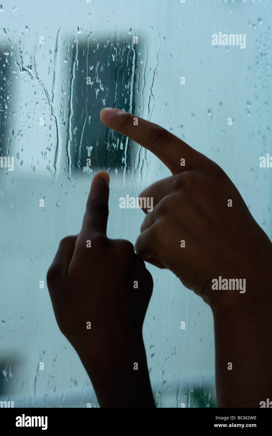 Genitore e bambino tracing gocce di pioggia sulla finestra con le dita, vista ritagliata delle mani Foto Stock