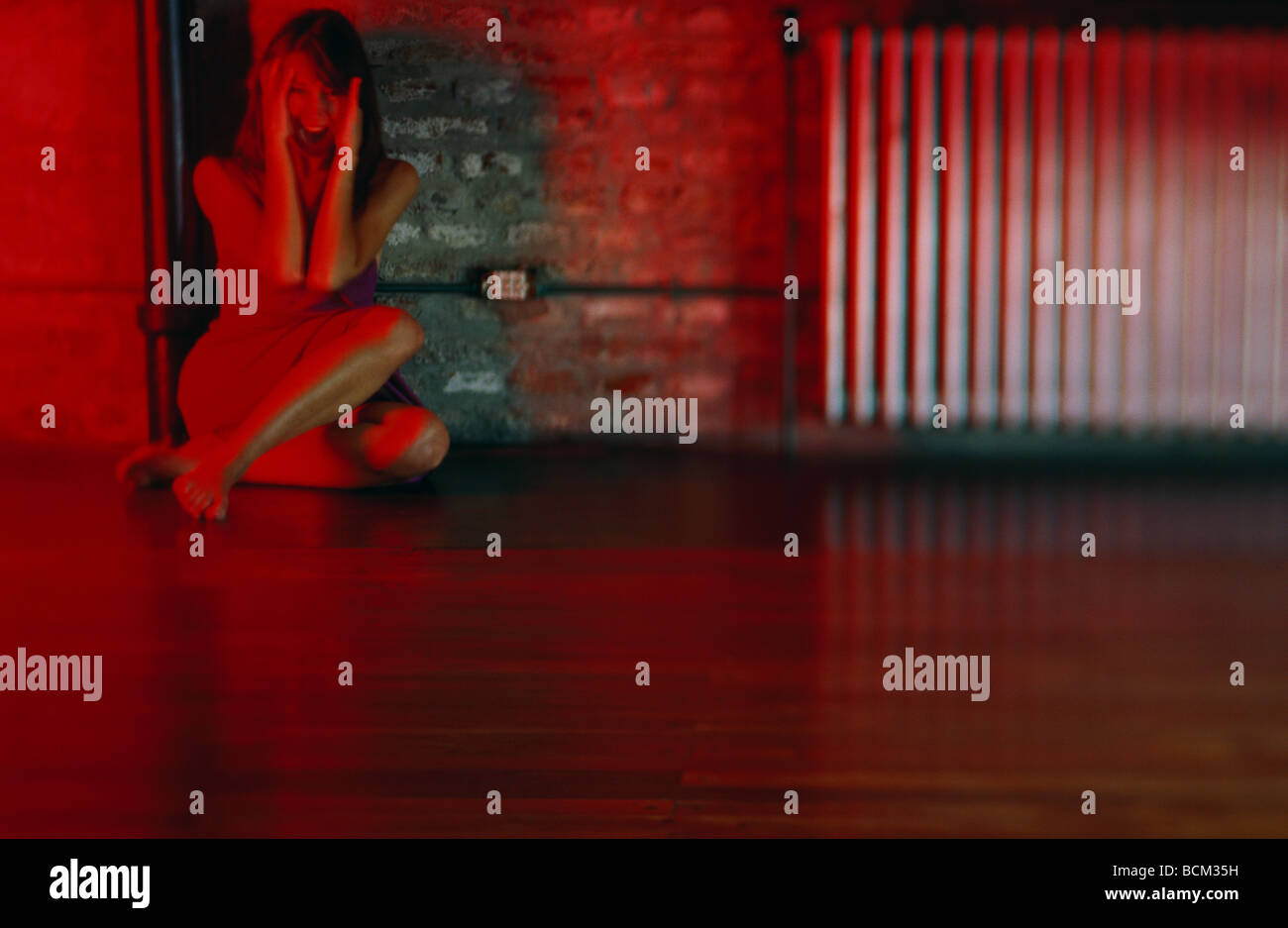 Donna seduta sul pavimento, appoggiata contro il muro, urlando Foto Stock