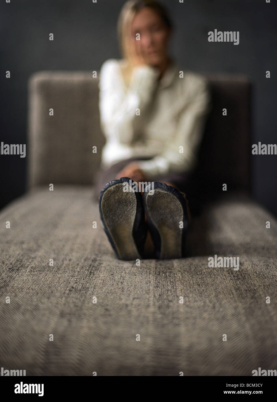 Giovane donna seduta su un divano, tenendo la testa, concentrarsi sulla suola delle scarpe Foto Stock