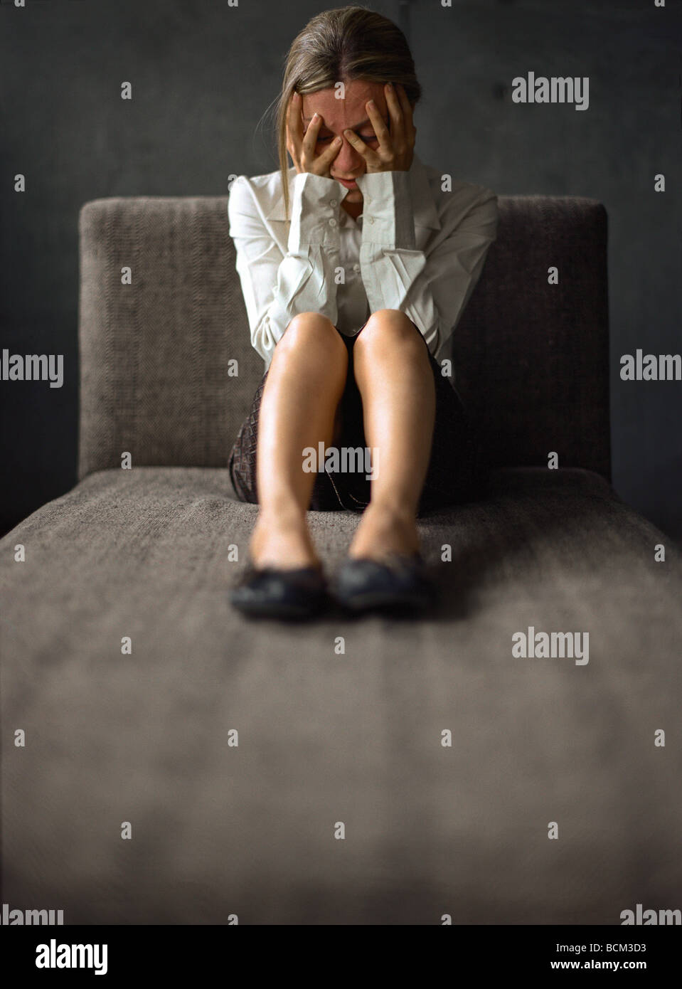 Giovane donna seduta su un divano, tenendo la testa Foto Stock