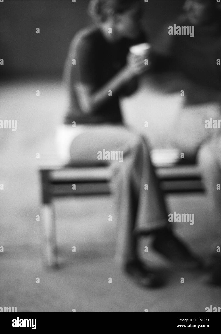 Giovane seduto su un banco di lavoro, a bere caffè, sfocato Foto Stock
