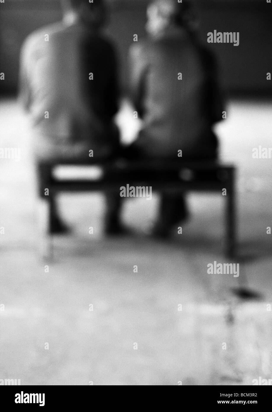 L uomo e la donna seduta sul banco, parlando, vista posteriore, sfocato Foto Stock
