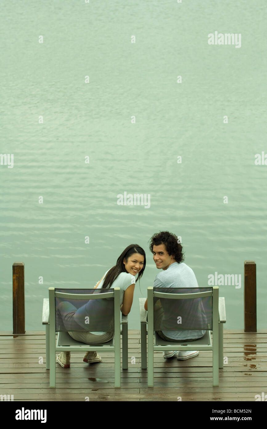 Giovane seduto sul dock, sorridente sulla spalla in telecamera Foto Stock
