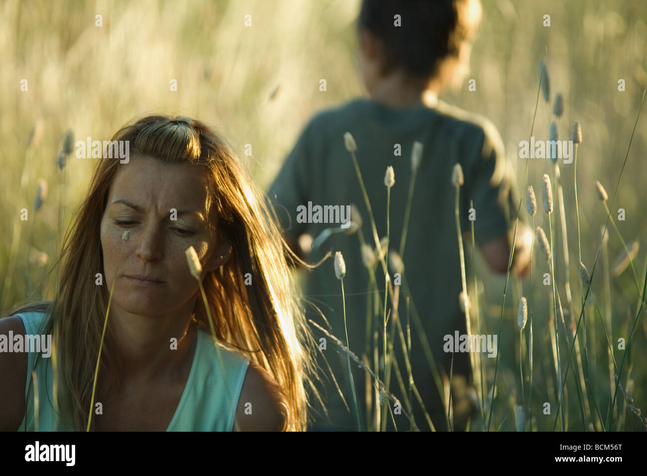 La donna nel campo di erba alta, solcando brow, figlio di esplorare in background Foto Stock
