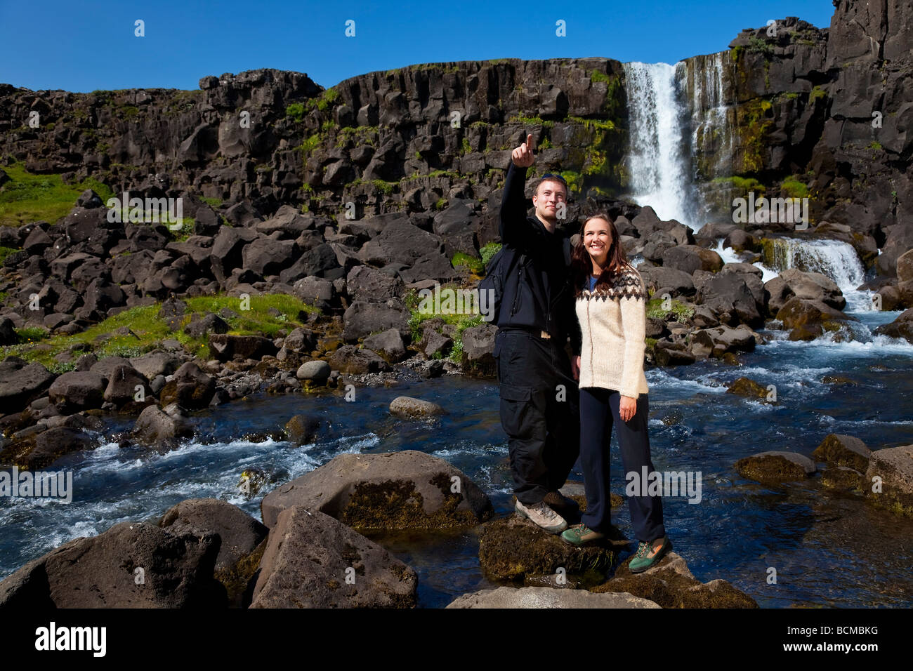Una giovane coppia che attraversa un ruscello di montagna mentre fuori camminando insieme girato in location in Islanda Foto Stock