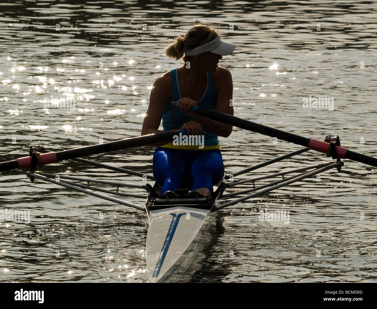 Sportivo da donna giovane barca a remi in barca in acqua al tramonto Foto Stock