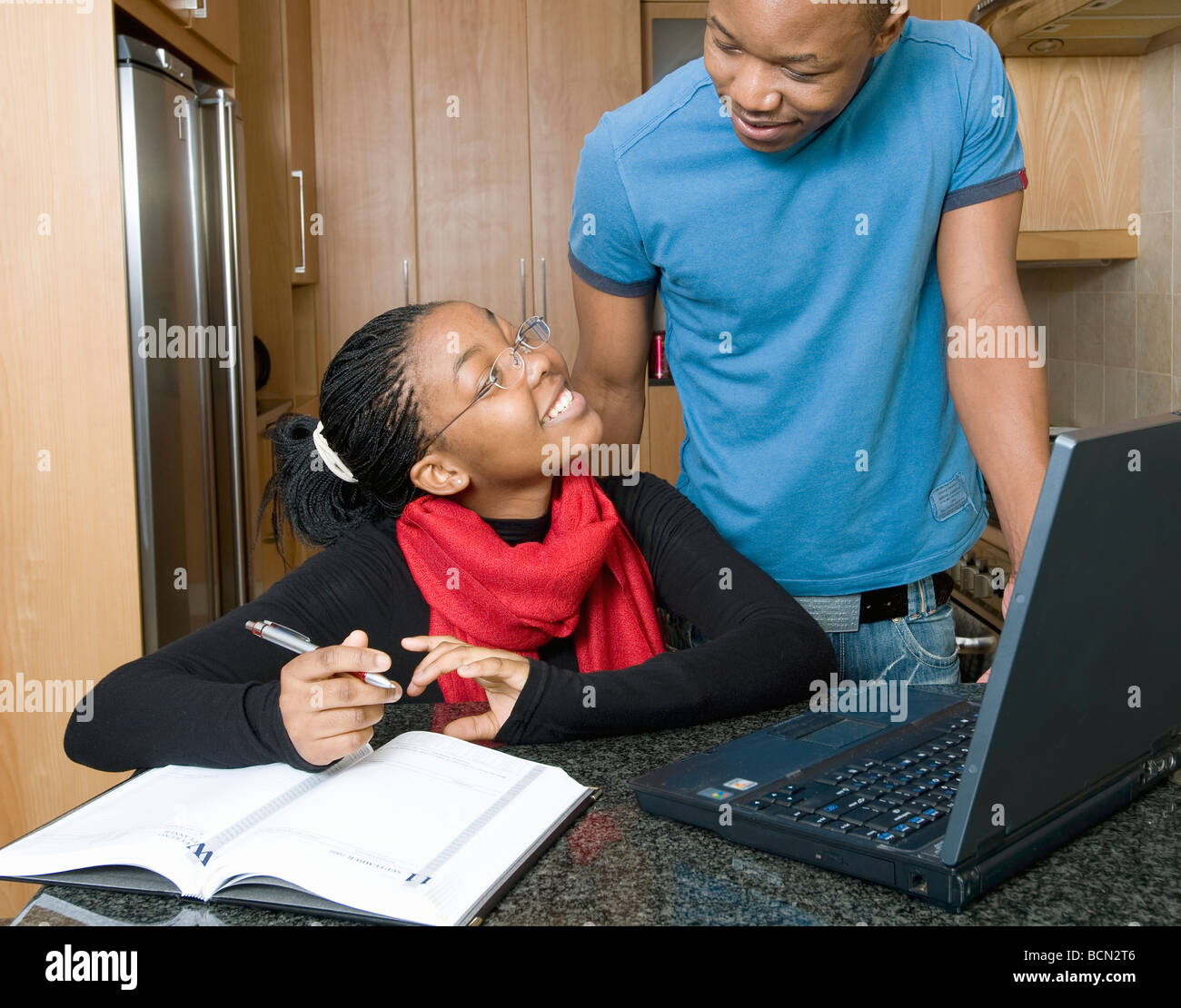 Una giovane donna guarda fino a un giovane uomo mentre lavora su un portatile a casa Foto Stock