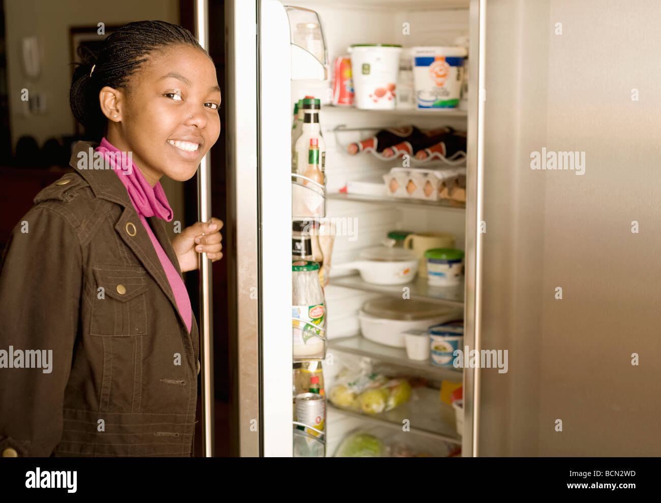 Una giovane donna si apre la porta del frigo Foto Stock