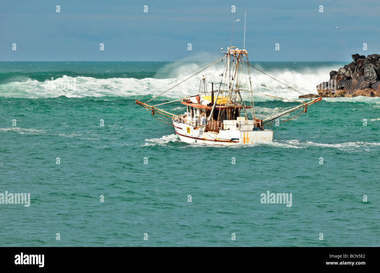 Barca da pesca si avvicina a mare mosso e si gonfia in entrata per l'oceano Foto Stock