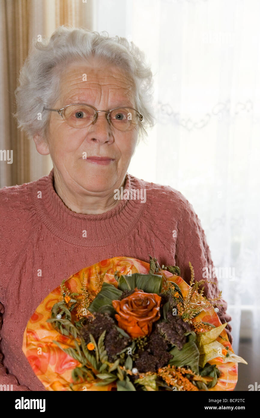 Frau in ihren Siebzigern steht im Wohnzimmer und hält einen Blumenstrauß künstlichen Foto Stock