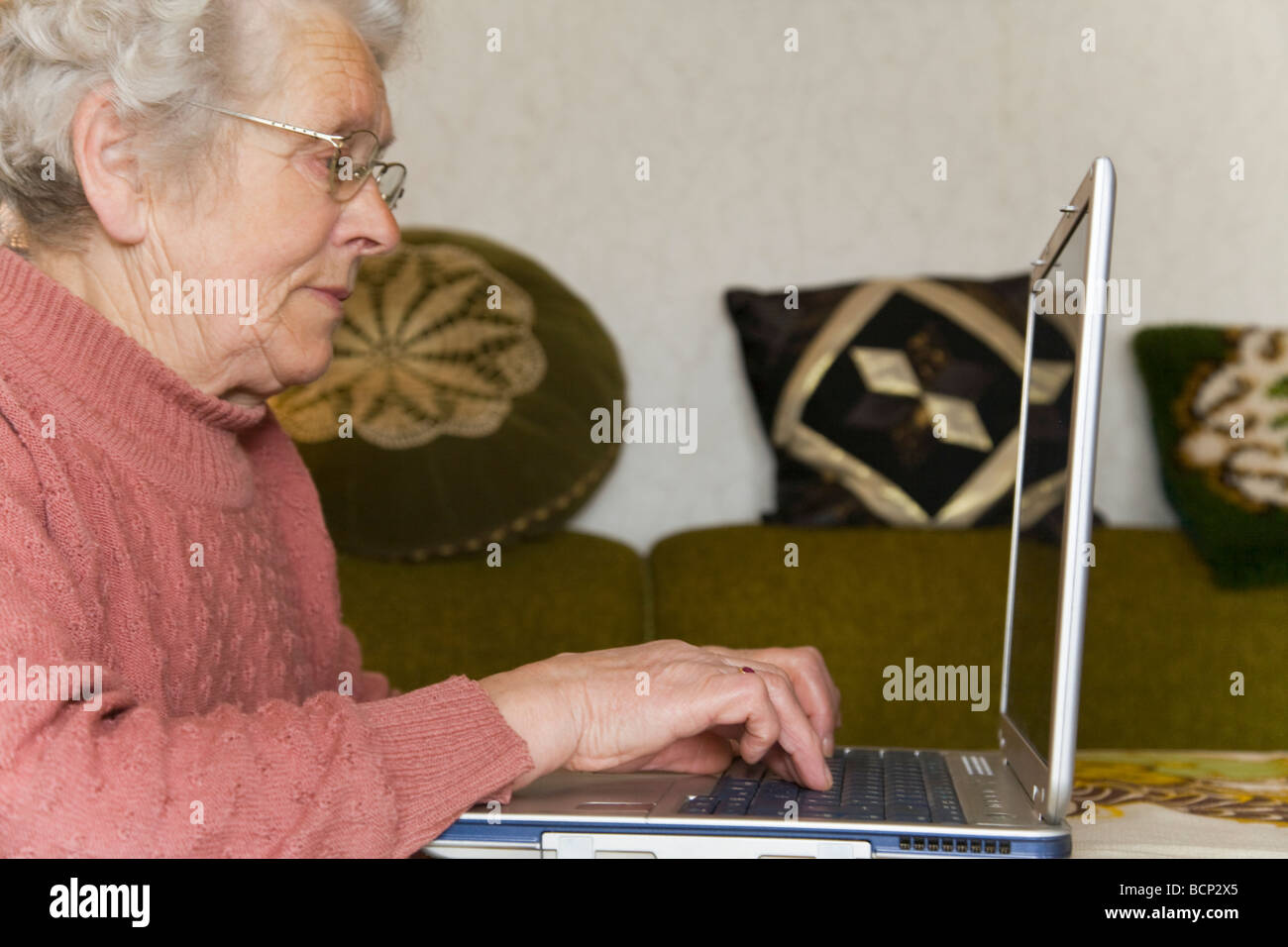 Frau in ihren Siebzigern sitzt im Wohnzimmer am Laptop Foto Stock