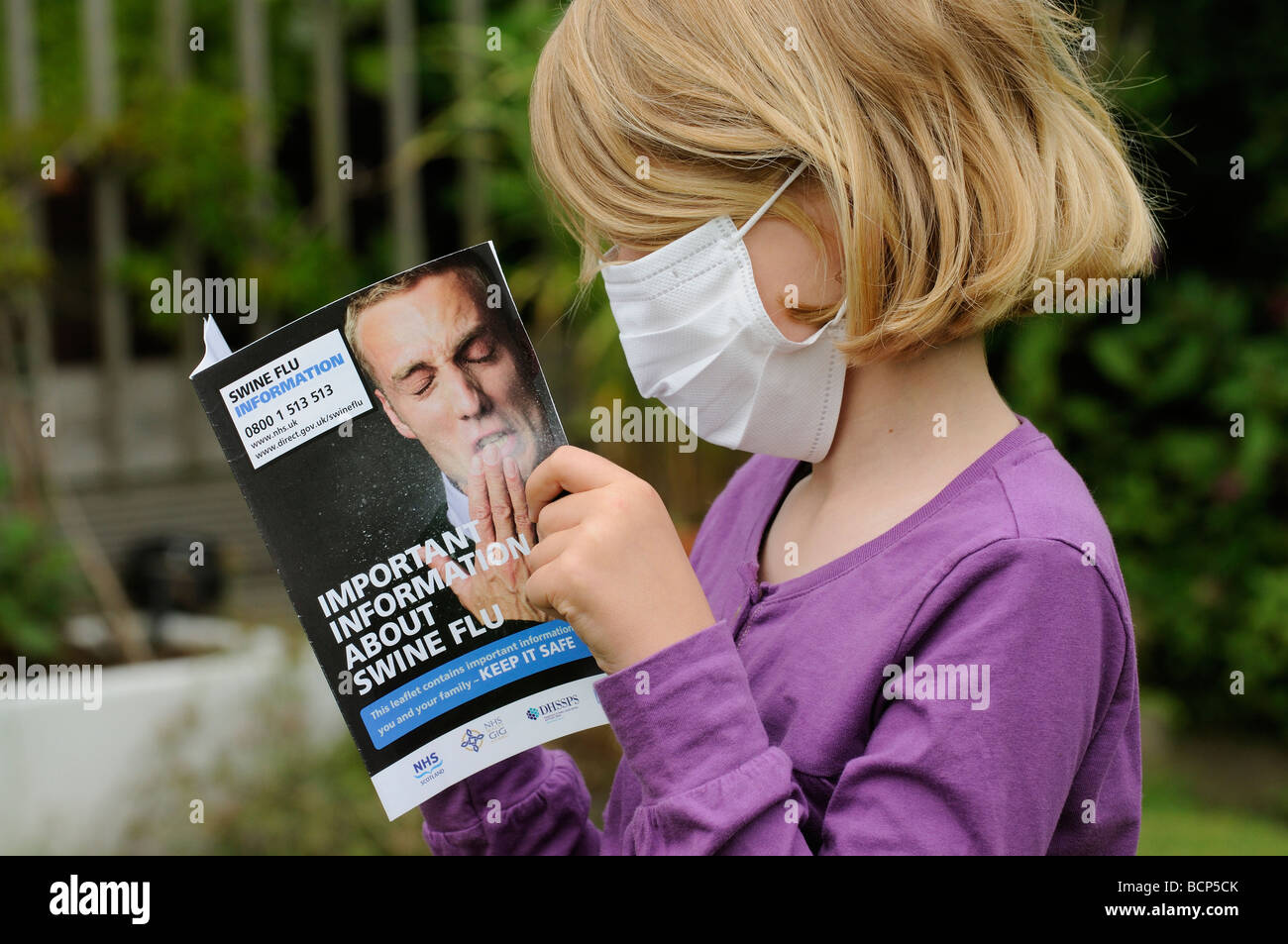 Influenza suina opuscolo informativo in lettura da una bambina indossa una maschera di medico Foto Stock