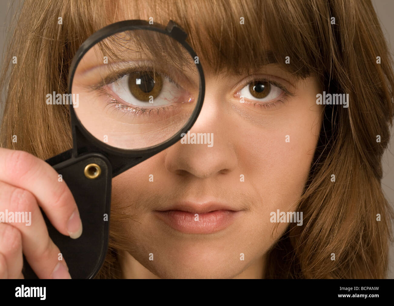 Una giovane donna ventenne guardando attraverso una lente di ingrandimento Foto Stock