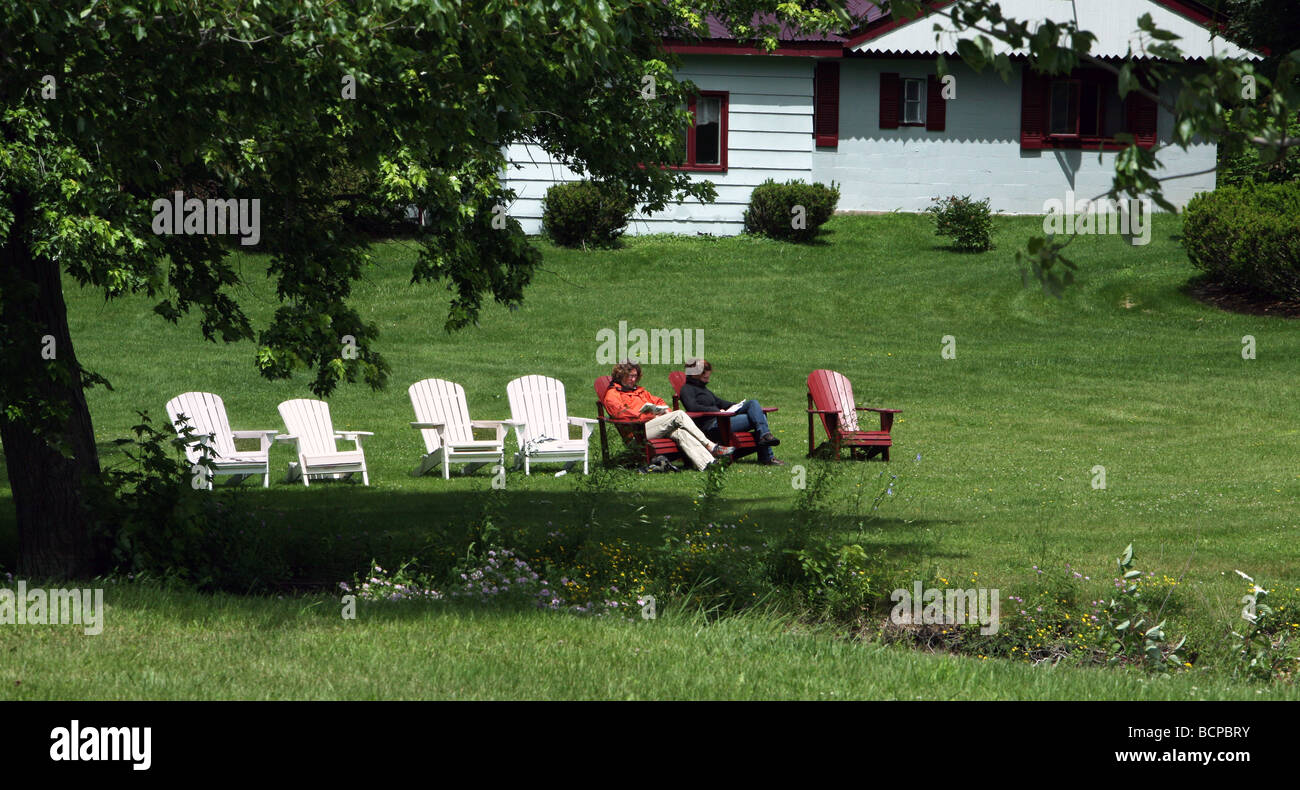 Gli ospiti seduti e lettura in Adirondack sedie in fila in un resort Adirondack State Park New York Lake Champlain. Foto Stock