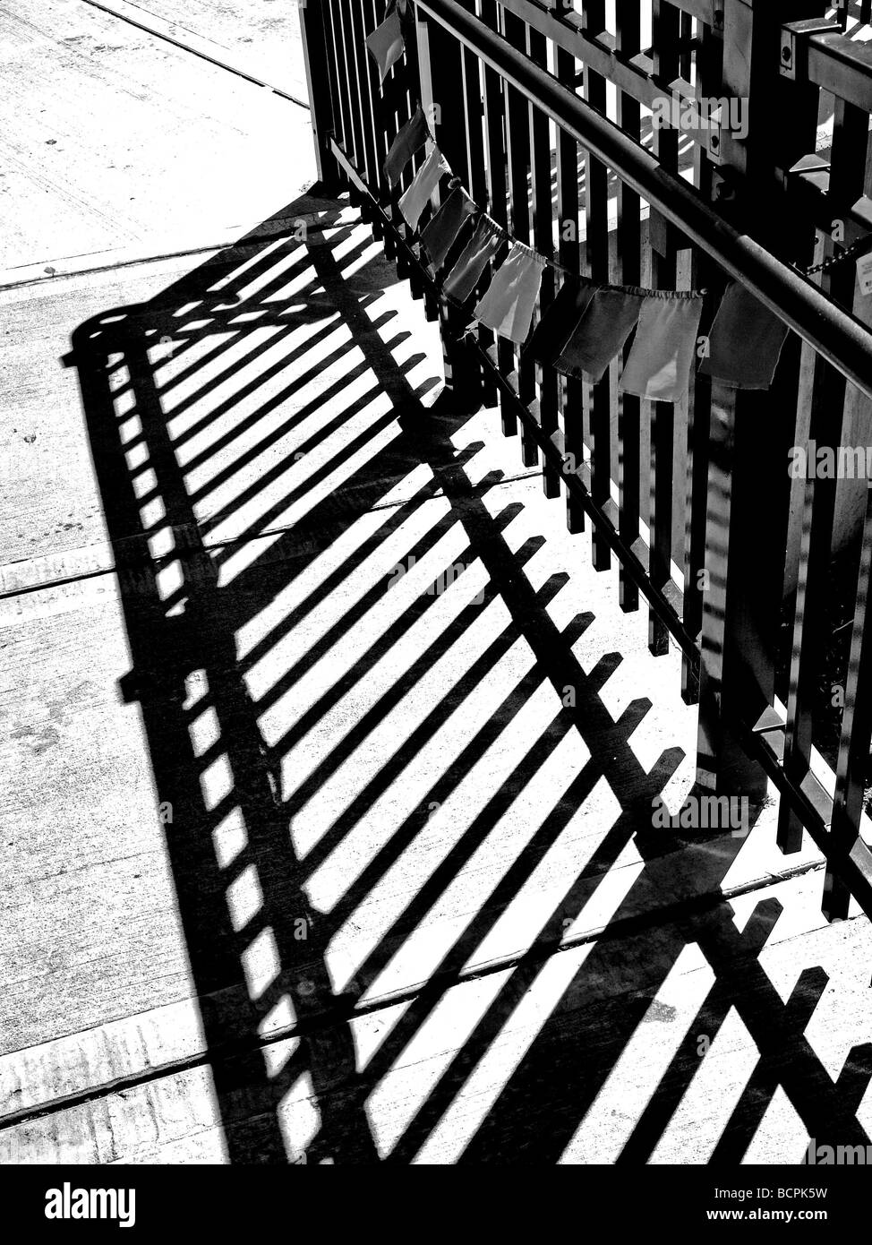 Recinzione metallica in bianco e nero con ombra scura di pali da recinzione e rotaie, sul cemento Foto Stock