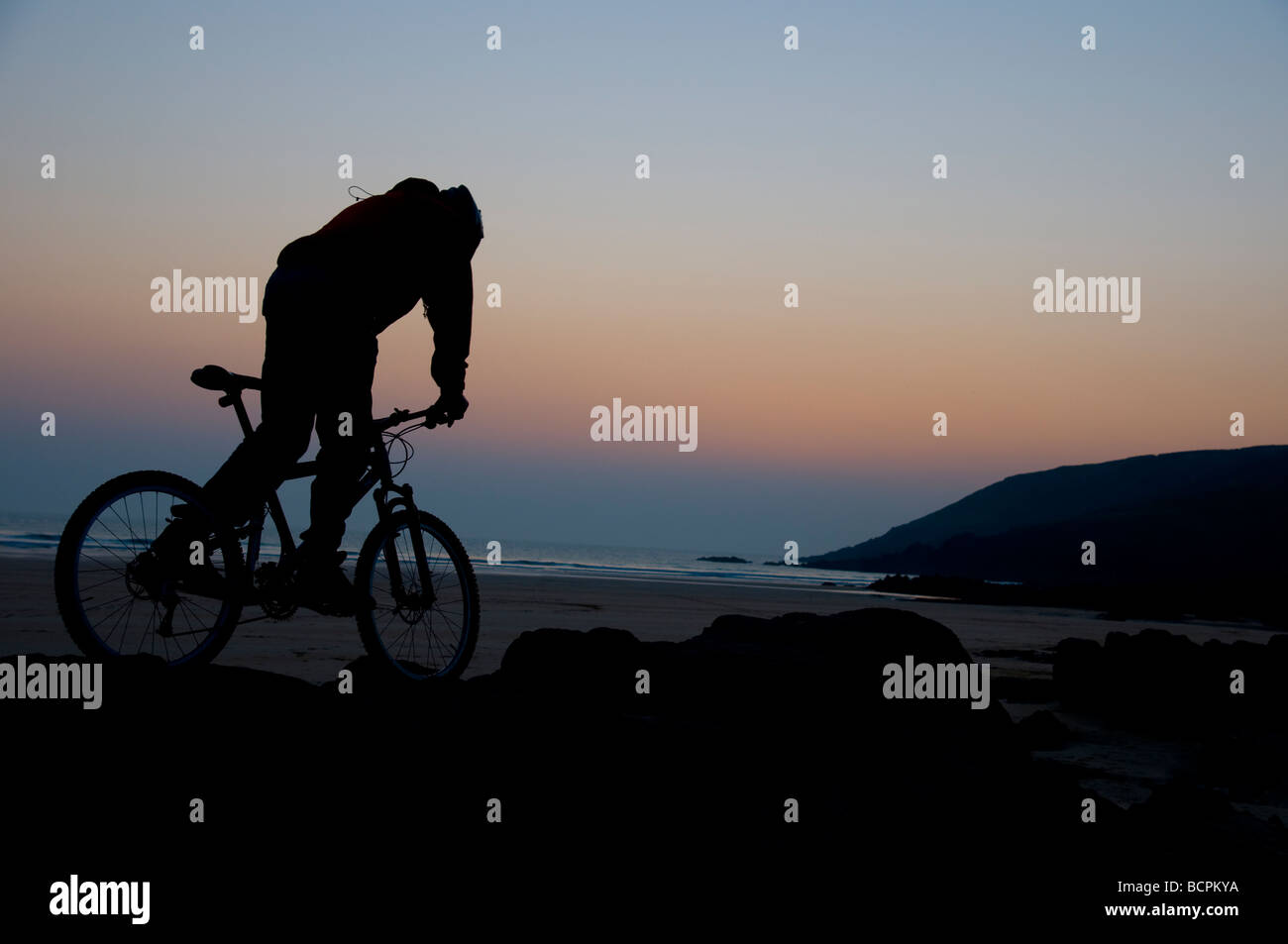 Mountain Biker a Freshwater West Beach al tramonto che viaggiano lungo le rocce Foto Stock