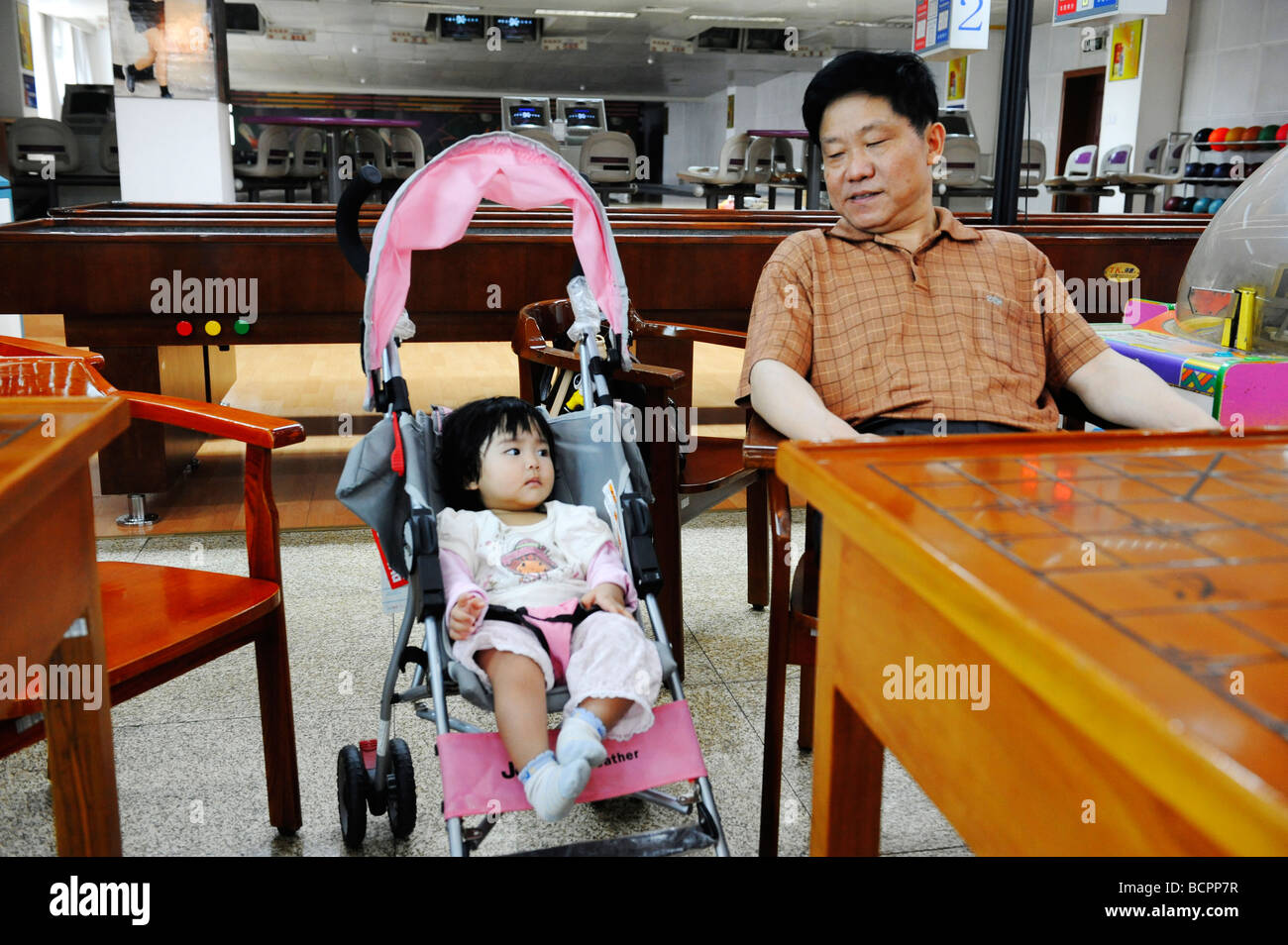 Padre e figlia in passeggino in appoggio in una galleria locale accanto a una pista da bowling, Chengdu nella provincia di Sichuan, in Cina Foto Stock
