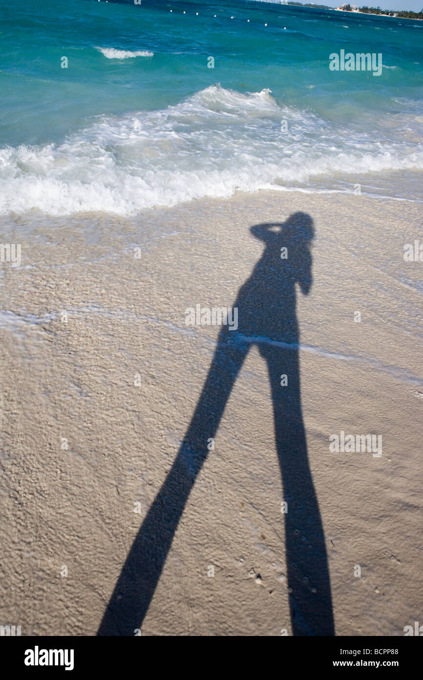 Una persona in possesso di una fotocamera e scattare una foto sulla spiaggia di sabbia di oro e blu brillante acqua Foto Stock