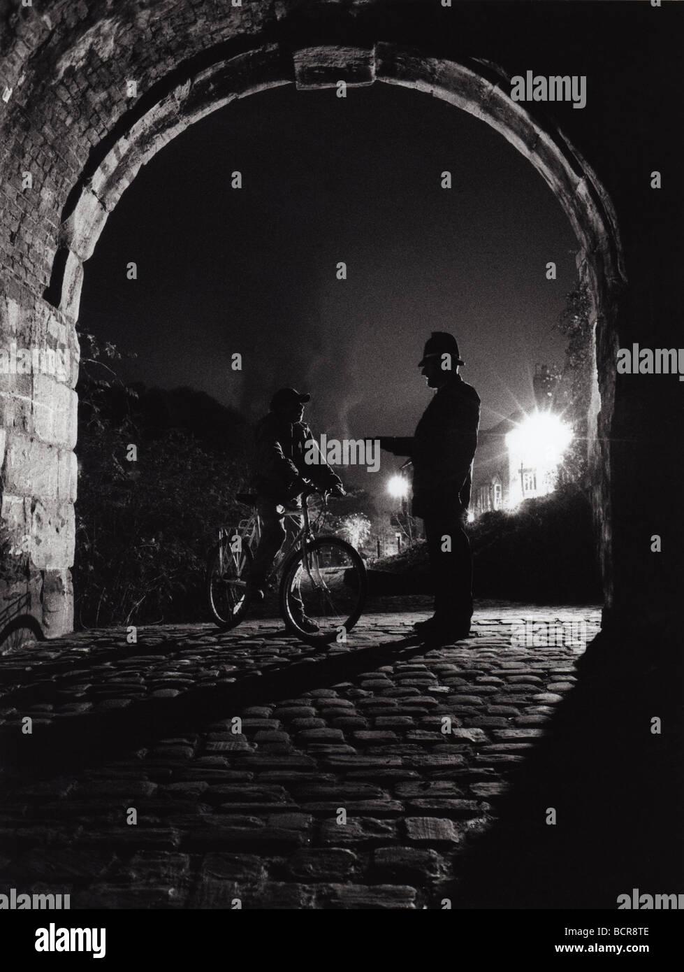 Ufficiale di polizia britannica che tiene la torcia ferma giovane ragazzo in bicicletta di notte Gran Bretagna UK 1980s poliziotto stabile servizio di polizia locale di notte Foto Stock