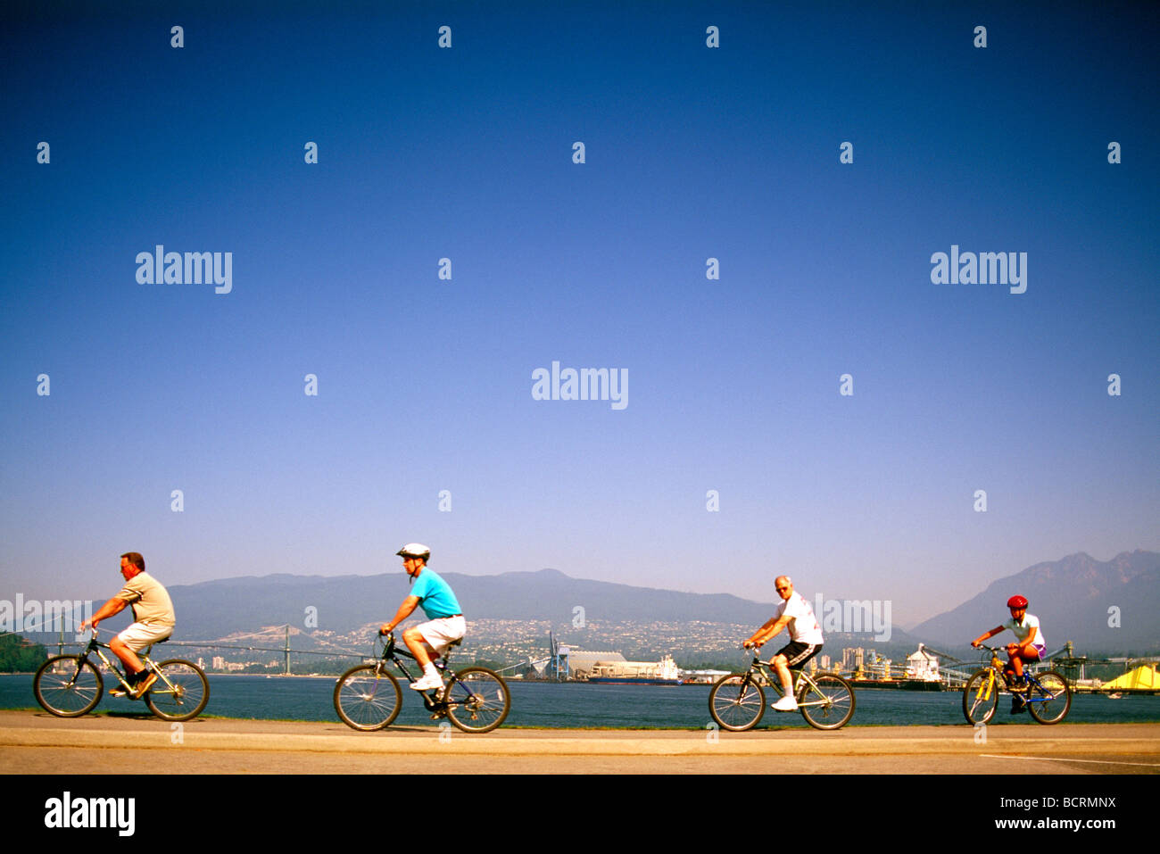Quattro i ciclisti di pedalare sulla Stanley Park Seawall lungo ingresso Burrard Vancouver British Columbia Canada Foto Stock