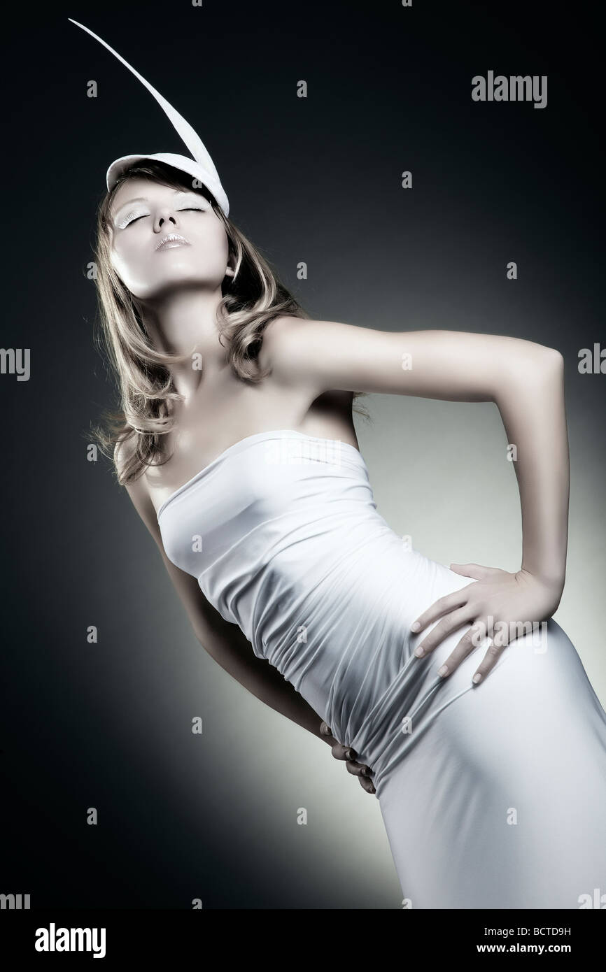 Moda colpo di una giovane donna che indossa un abito bianco e un cappello piumato Foto Stock