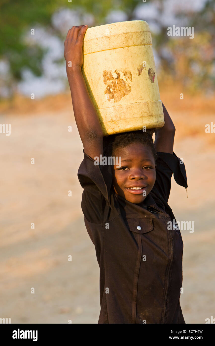 Bambino locale trasporto tanica in plastica con acqua potabile sulla testa, Zambia, Africa Foto Stock