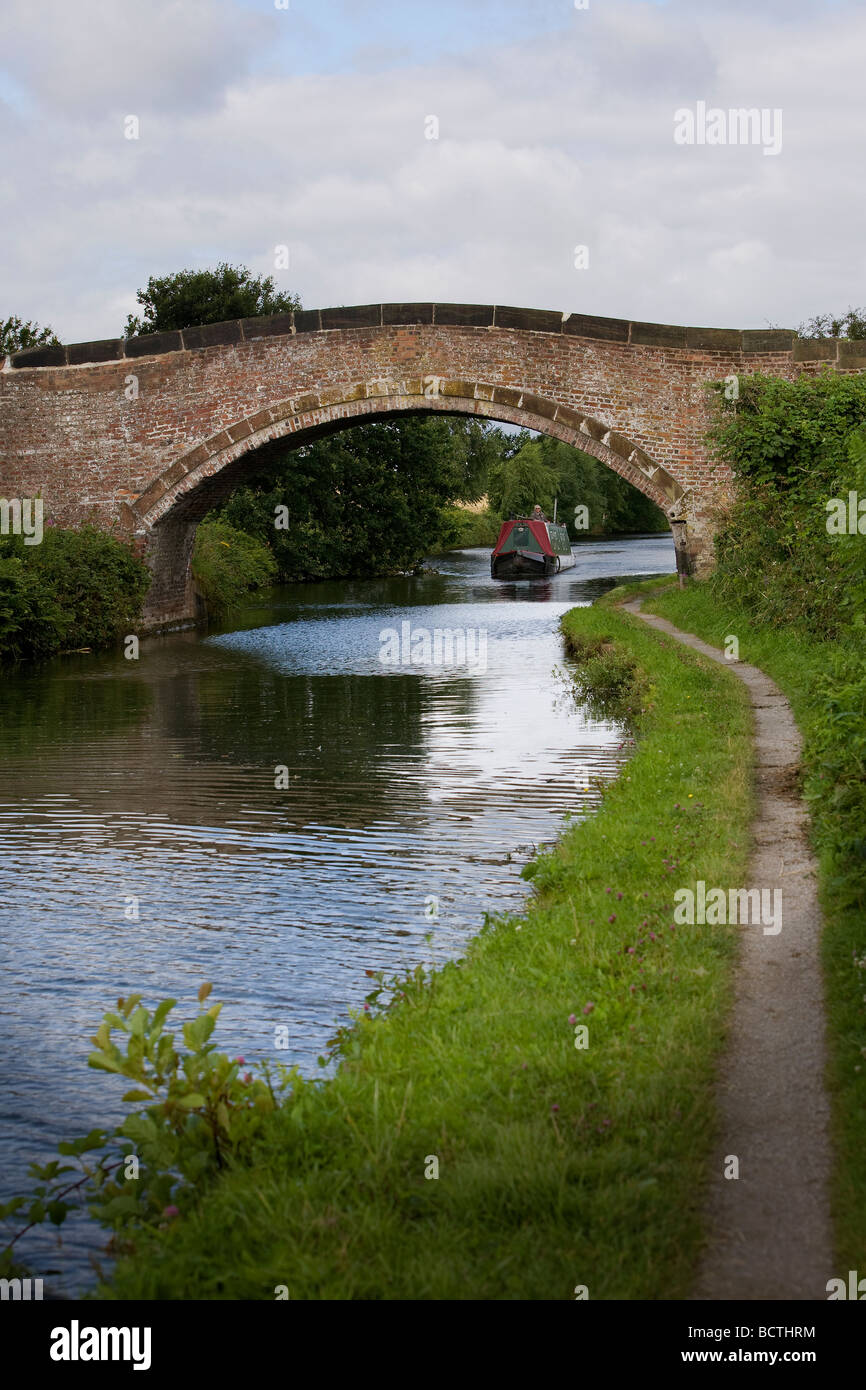 Una stretta imbarcazione naviga lungo Bridgewater Canal e passa sotto un ponte arcuato Foto Stock