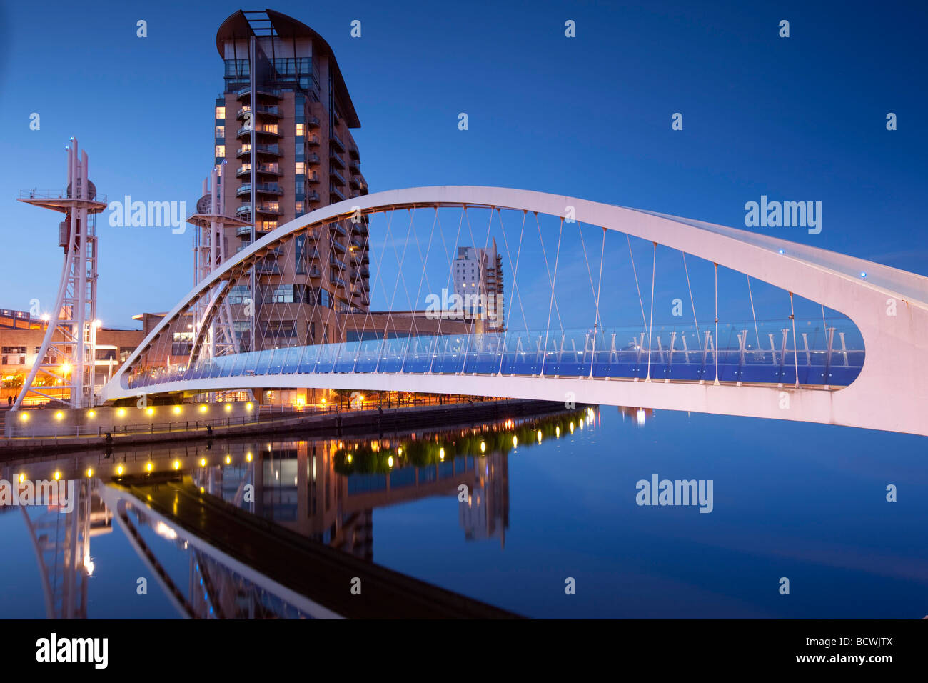 Un ponte pedonale a Salford Quays, Manchester visto al crepuscolo contro un cielo blu con le luci. Lowry Centre shopping. Foto Stock