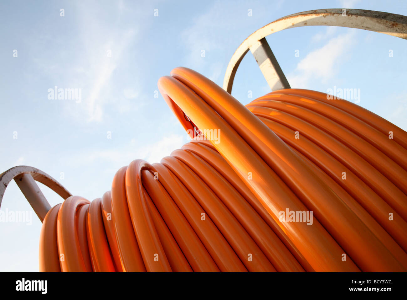Il cavo arancione per le connessioni a banda larga su un cavo di acciaio tamburo contro un cielo blu. Foto Stock Il cavo arancione per le connessioni a banda larga su un cavo di acciaio tamburo contro un cielo blu. Foto Stock