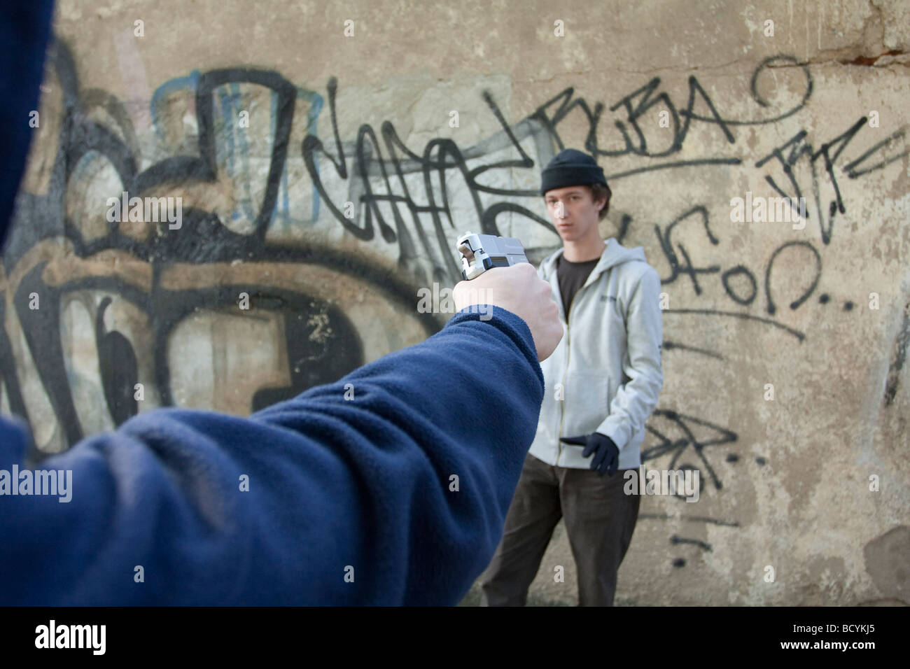 Uomo in giacca con cappuccio pistola di puntamento al rivale Foto Stock